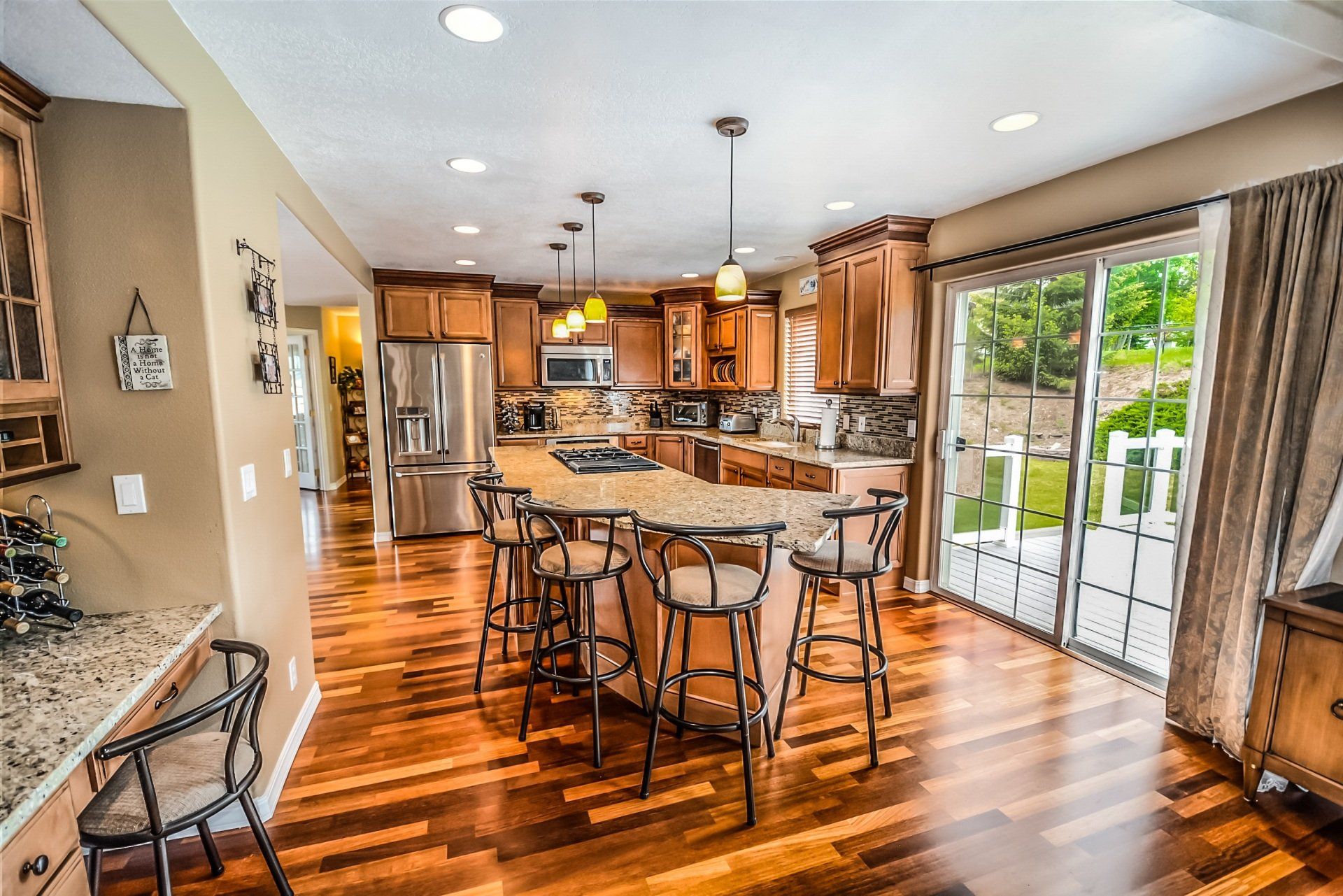 Wooden-floored kitchen with a large island, brown cabinets, stainless steel appliances, and a sliding glass door to a patio.