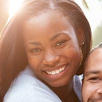 Smiling woman, close-up, outdoors. She is embracing someone out of frame. Bright sunlight.